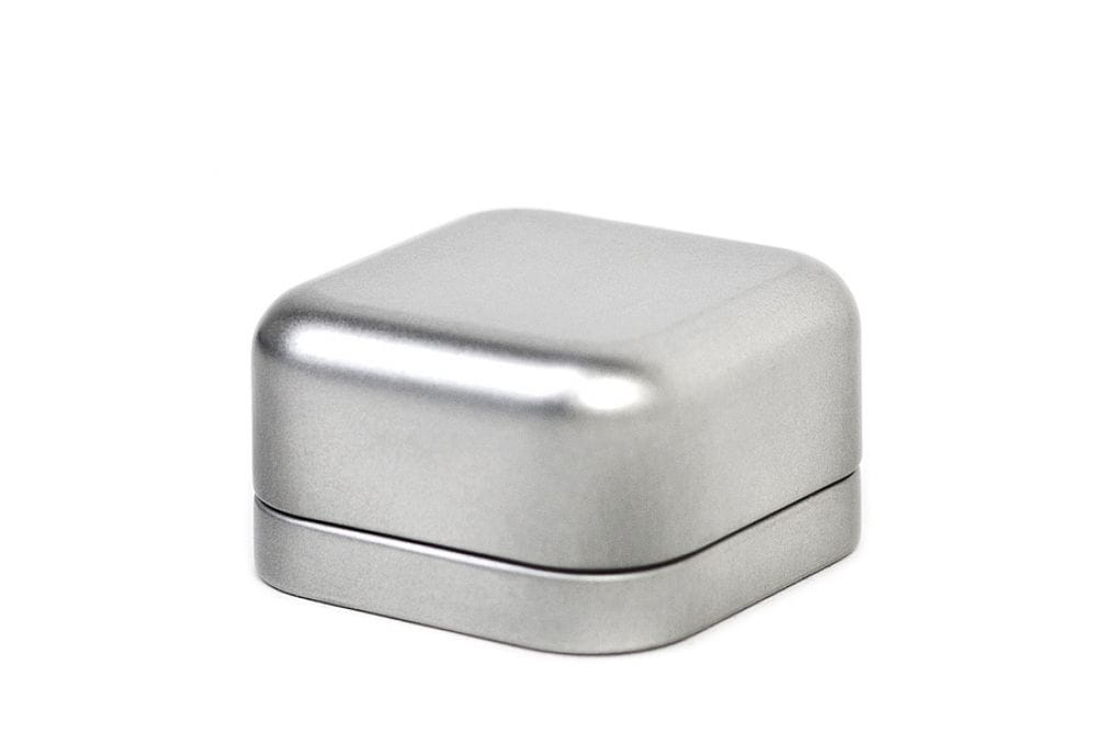 Geschlossene kleine quadratische Metalldose in Silber, mit aufgesetztem Deckel, neutraler weißer Hintergrund.